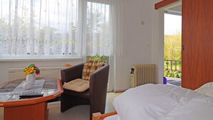 A hotel room with a bed, a chair with a cushion, a table with a vase of flowers, and a window with sheer curtains. - Gemutlicher Bungalow in Freest (Kröslin)