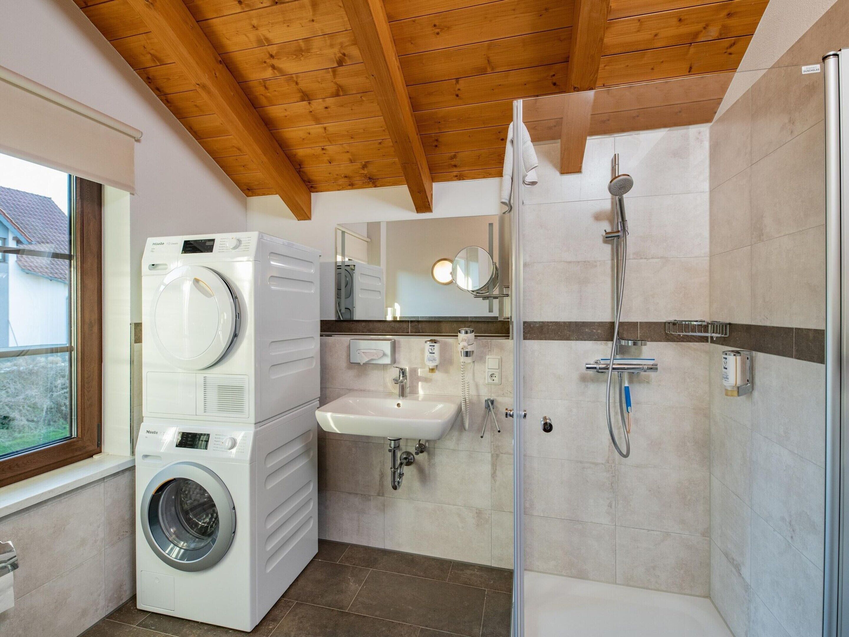 Ein modernes Badezimmer mit Waschmaschine, Waschbecken, Spiegel und Dusche.