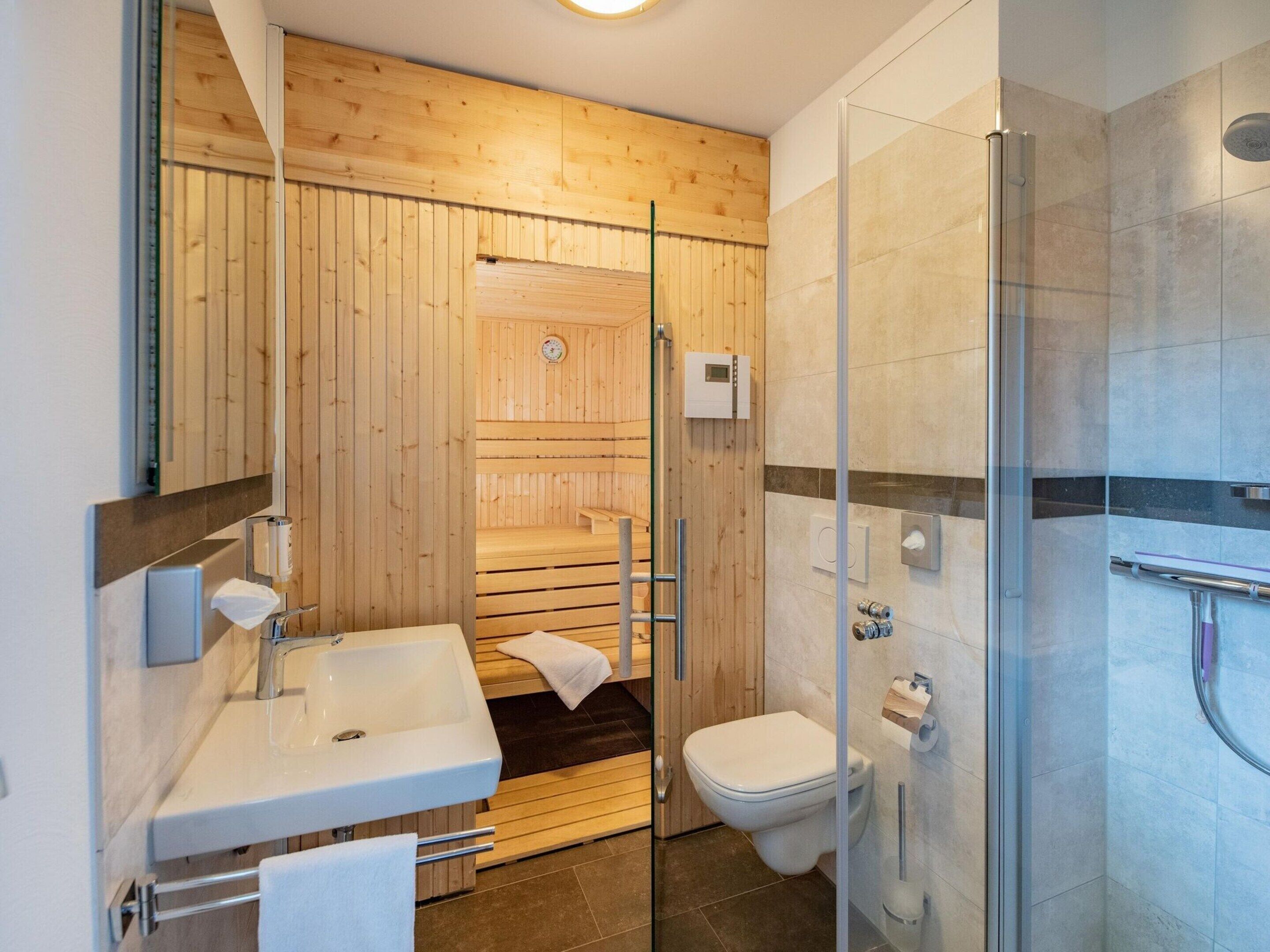 A modern bathroom with a wooden sauna, a glass-enclosed shower, and a white sink.