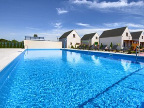 Ein Schwimmbecken mit Liegestühlen und ein weißes Gebäude mit grauem Dach im Hintergrund.