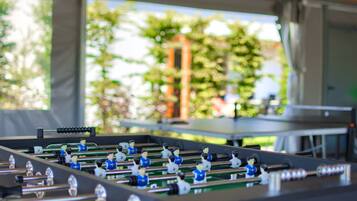 A foosball table in a room with a view of trees and a table tennis table in the background.