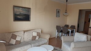 A living room with a sofa, two round tables, a dining table with chairs, and a painting on the wall. - Ferienanlage Orther Reede, Fehmarn-orth (Fehmarn)