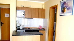 A compact kitchen with wooden cabinets, a black countertop, and a stainless steel range hood. - Ferienanlage Orther Reede, Fehmarn-orth (Fehmarn)