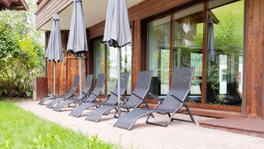 A row of sun loungers with umbrellas, a wooden fence, and a glass door leading to a garden.