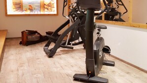 A stationary bike in a room with a wooden floor, a mirror on the wall, and a painting.