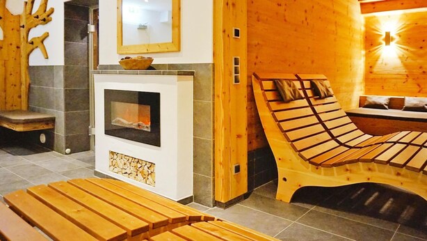 A wooden interior with a fireplace, a bed, and a bench.