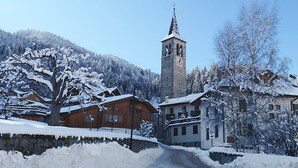 A snow-covered village with a prominent church tower, wooden buildings, and a road leading through the village. - Apartments Casa Caritro, Cusiano di Ossana (Ossana)