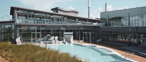 Un edificio moderno con un amplio espacio de piscina, que incluye un jacuzzi y sillas de descanso.
