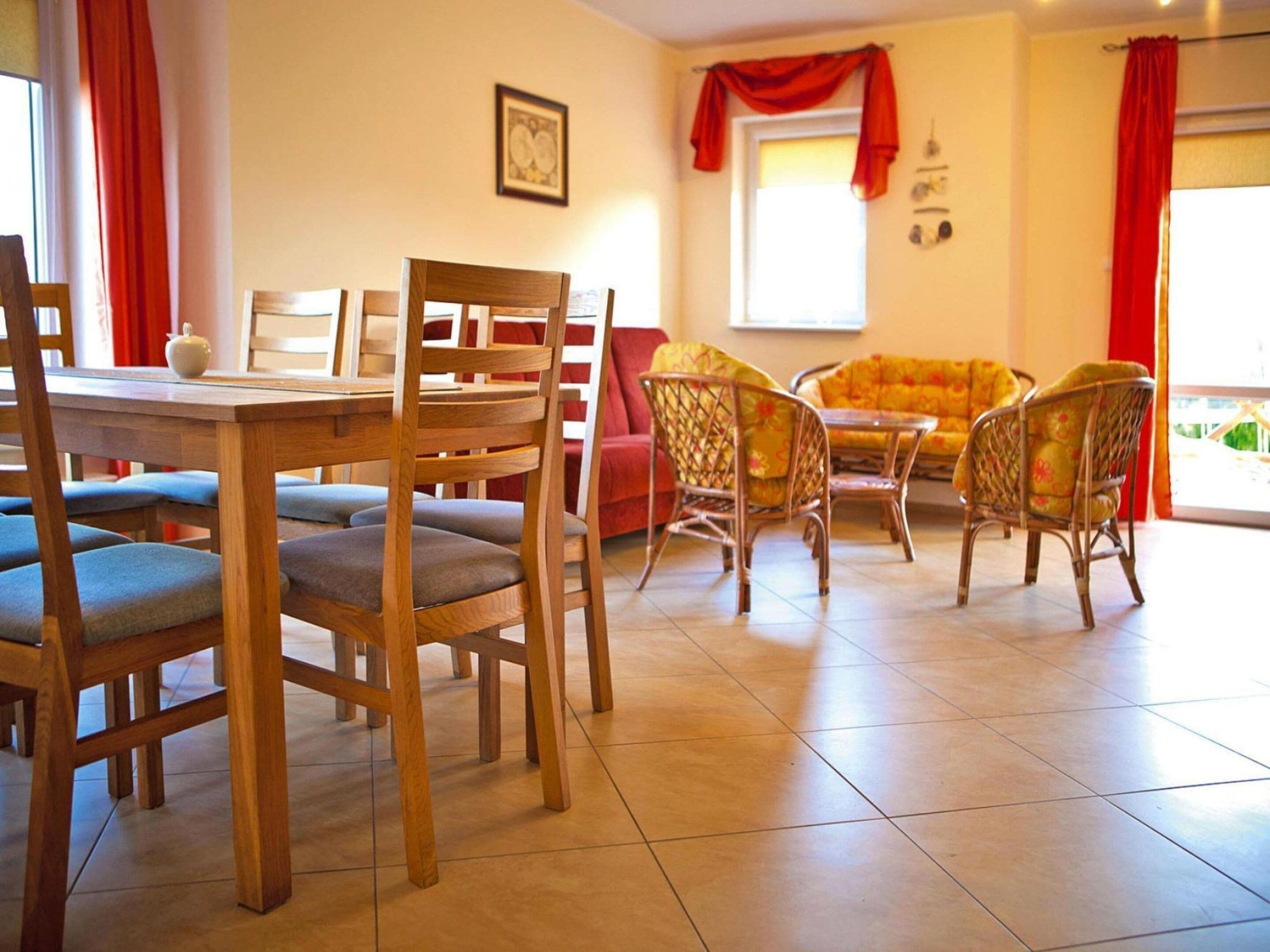 Un comedor con sillas de madera y una mesa, un sofá con cojines estampados y una ventana con cortinas rojas.
