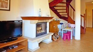 Ein Wohnzimmer mit Kamin, Fernseher, Esstisch mit Stühlen und einer Holztreppe.