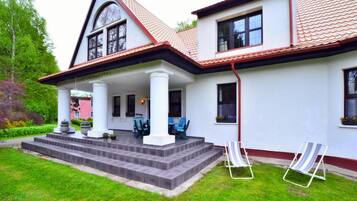 A two-story house with a covered porch, a red-tiled roof, and a well-maintained lawn.