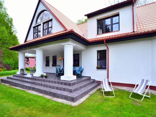 A two-story house with a covered porch, a red-tiled roof, and a white exterior.