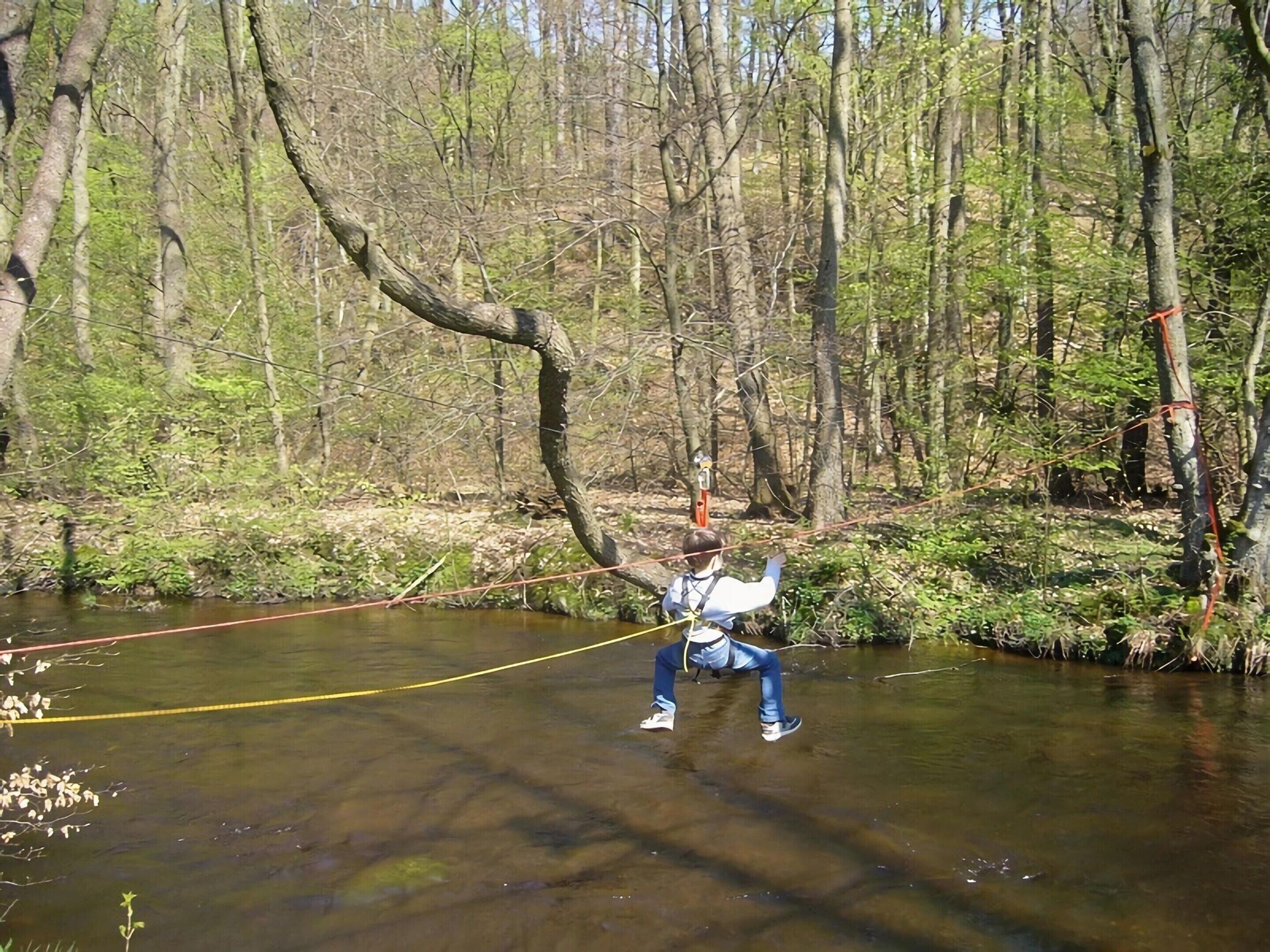 Una persona che vola su una zipline attraverso una zona boschiva con un fiume sottostante.