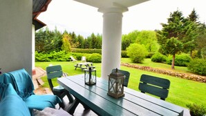 A patio with a wooden table and chairs, a cushioned bench, and a view of a well-maintained garden. - Holiday Villa With Fireplace and Private Garden (gmina Polanów)