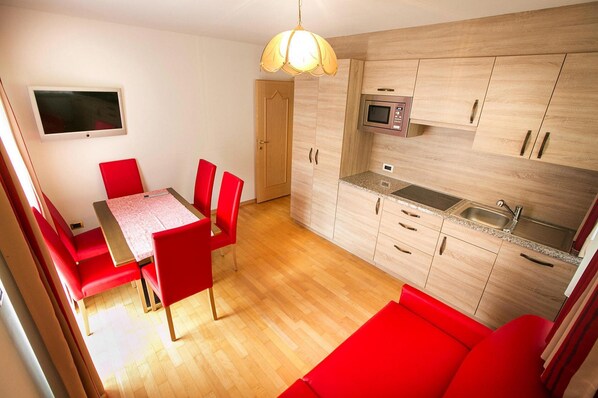 Une cuisine compacte avec des meubles en bois, un four à micro-ondes et un évier. On y trouve également un coin repas avec une table et des chaises rouges.