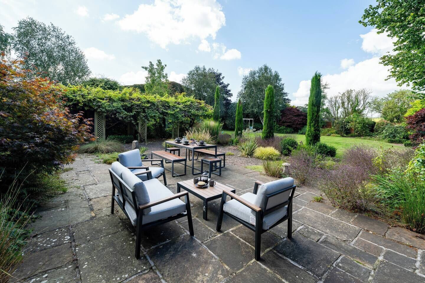 Une terrasse extérieure avec un sol en pierre, entourée d’une végétation luxuriante et de grands arbres.