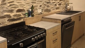 A kitchen with a stone wall, a stove, a sink, and wooden cabinets. - Tente Glamping Dans le Calme, Avec Piscine, Salle de Bain et Cuisine (Crespin)