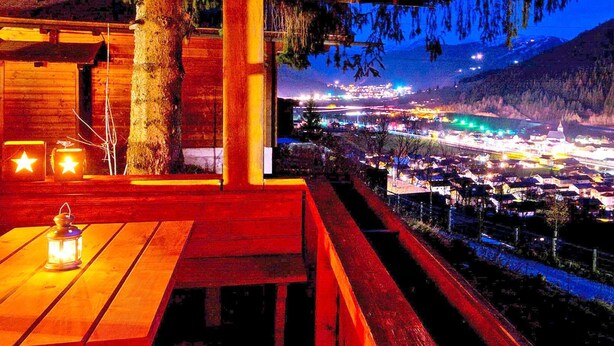 A wooden cabin with a bench and a table, overlooking a lit valley. - Chalet in Eben With Panoramic Mountain Views (Eben im Pongau)