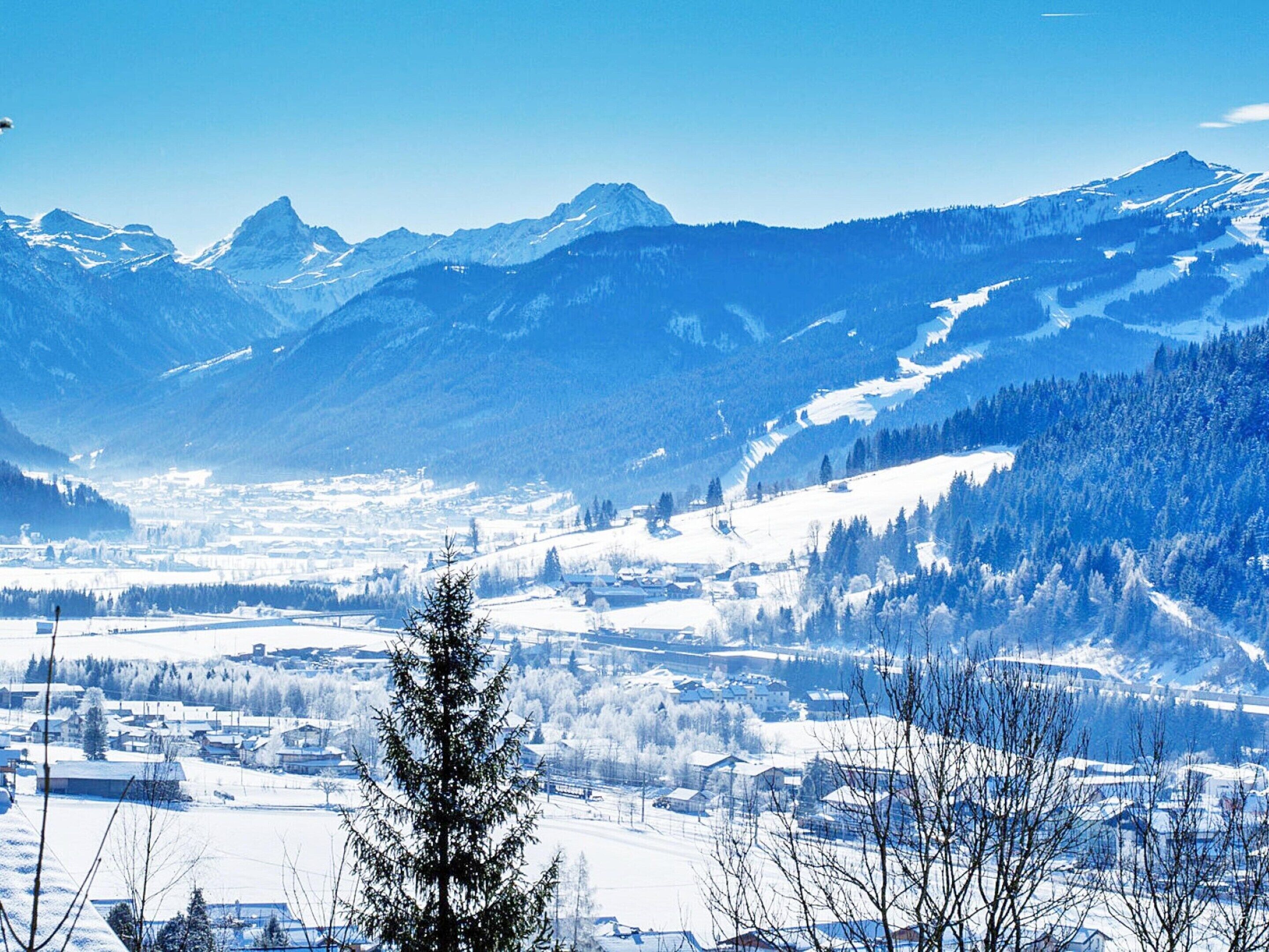 A mountainous landscape with snow-covered peaks and a valley with buildings.
