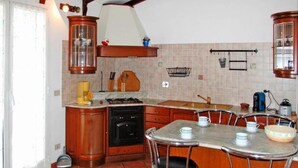 A kitchen with wooden cabinets, a stove, a sink, and a dining area with bar stools. - Apartment Agriturismo Le Mimose in Imperia (Imperia)