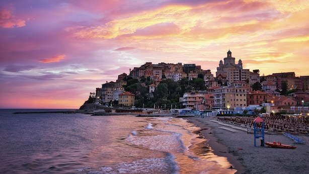 A coastal cityscape at sunset with buildings along the waterfront, a beach with umbrellas, and a clear sky. - Apartment Agriturismo Le Mimose in Imperia (Imperia)
