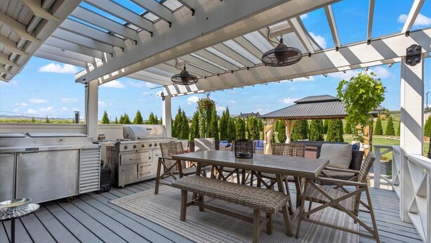 Un patio al aire libre con una parrilla, zona de estar y una pérgola con luces colgantes.