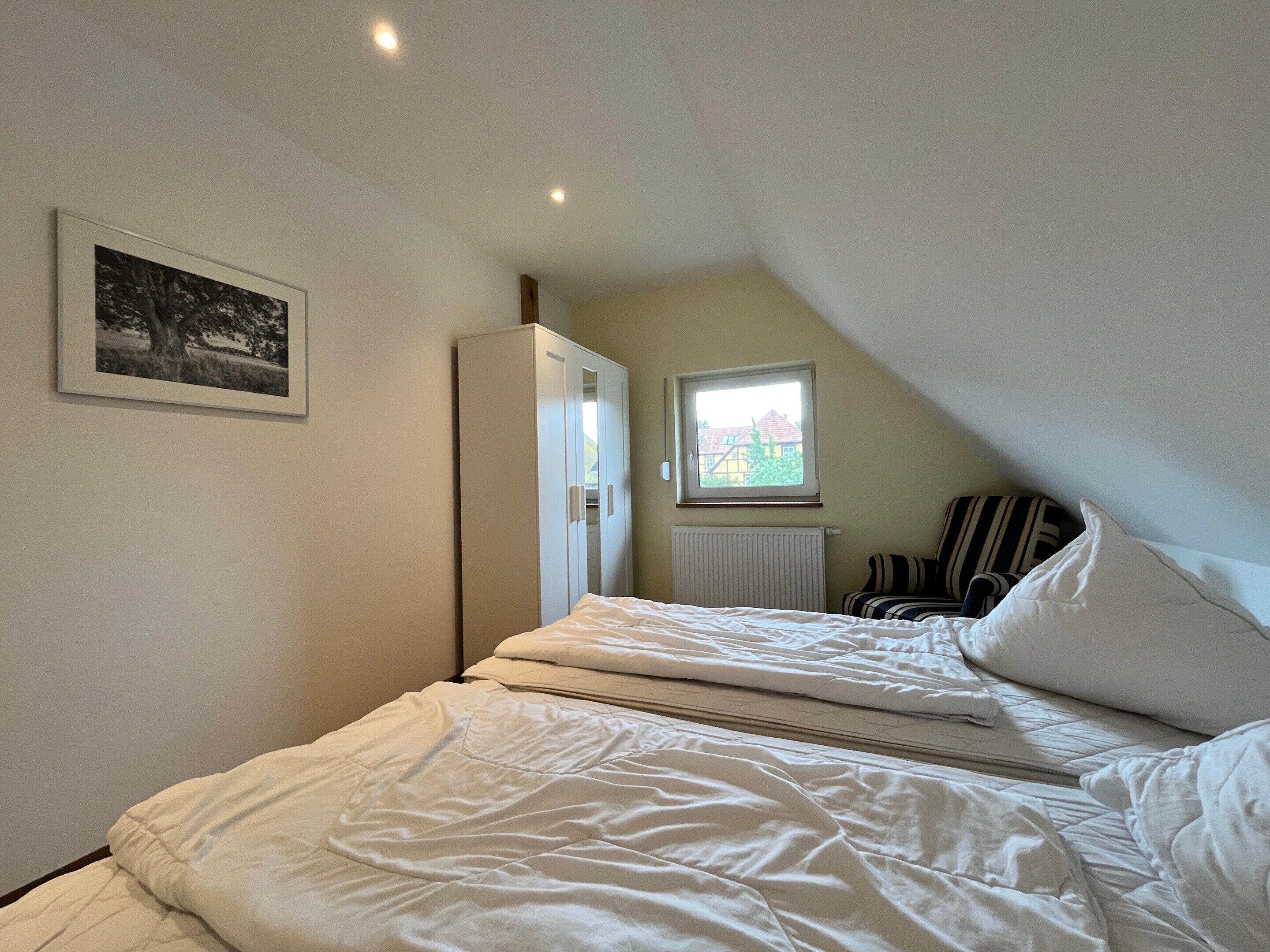 Een slaapkamer met een bed, een kast, een radiator, een raam en een ingelijst kunstwerk aan de muur.