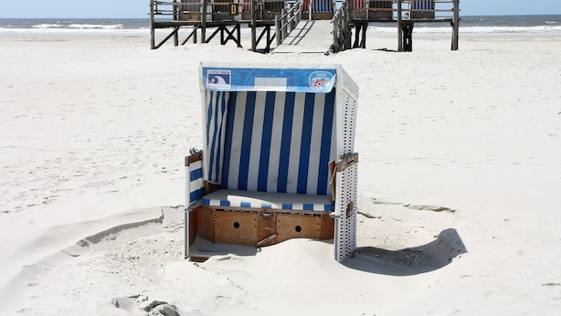 En strand med en række strandstole og en træbro.