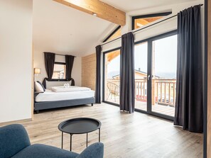 Quarto moderno com cama, uma mesinha e varanda com vista.