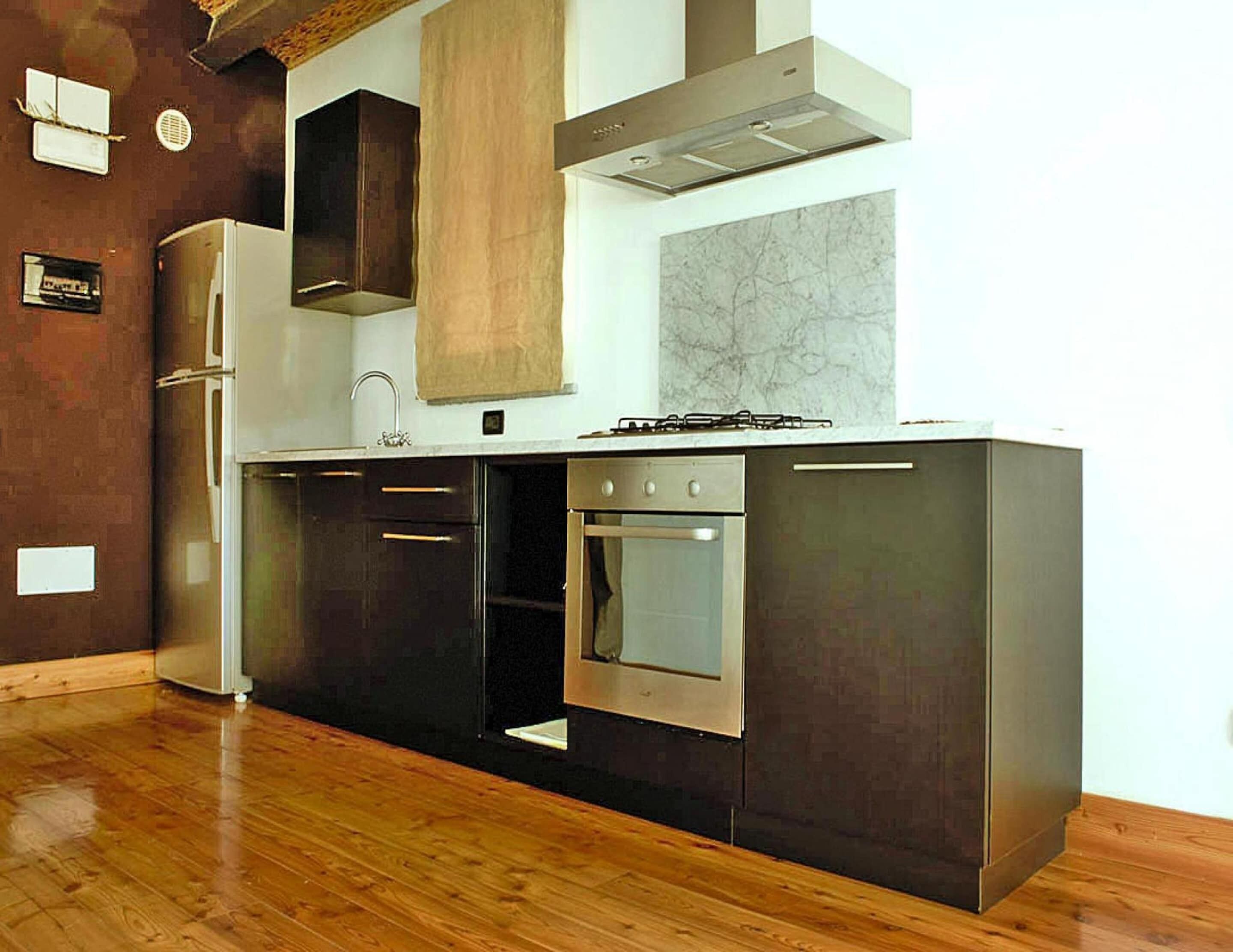 Une cuisine moderne avec des meubles de couleur sombre, des appareils en acier inoxydable et un plancher en bois.