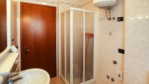 A bathroom with a wooden door, a white sink, a glass shower enclosure, and a wall-mounted heater. - Residence Villaggio Lido del Sole 1, Bibione (San Michele al Tagliamento)