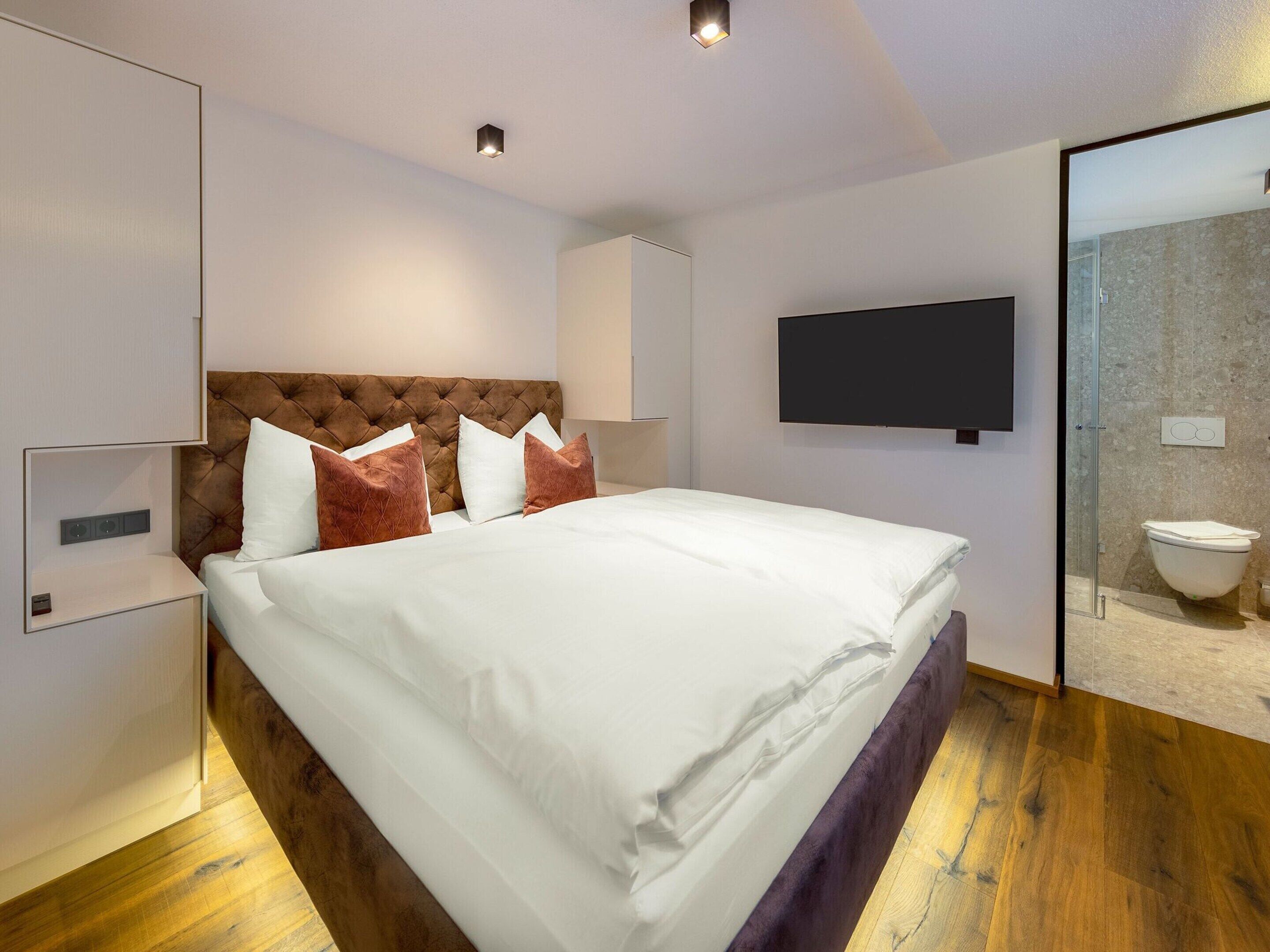 Une chambre d’hôtel moderne dotée d’un grand lit, d’un téléviseur à écran plat, d’une douche en verre et d’un plancher en bois.