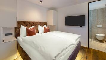 Une chambre d’hôtel moderne dotée d’un grand lit, d’un téléviseur à écran plat, d’une douche en verre et d’un plancher en bois.