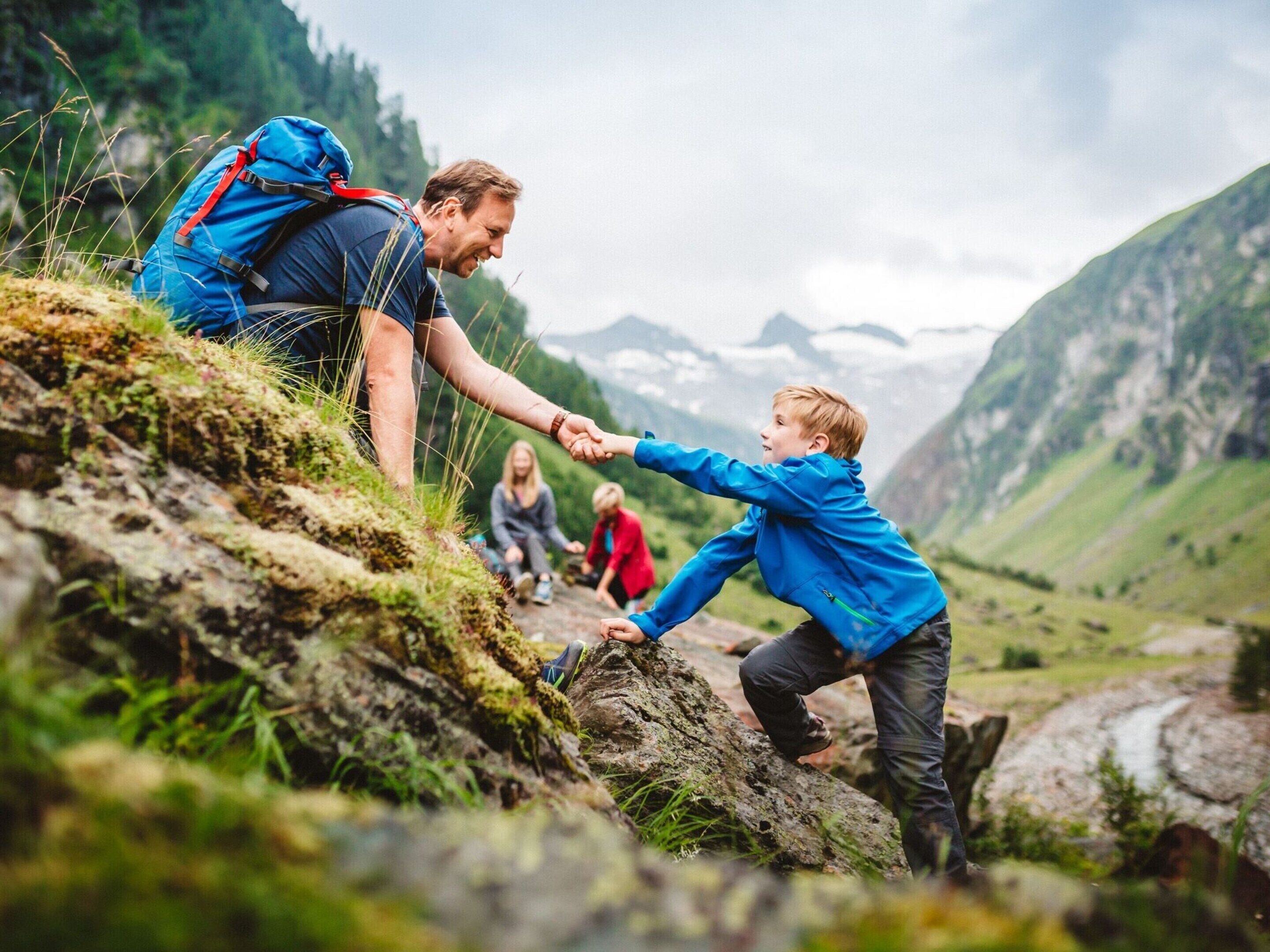 A mountainous landscape with a person helping a child climb a rock.