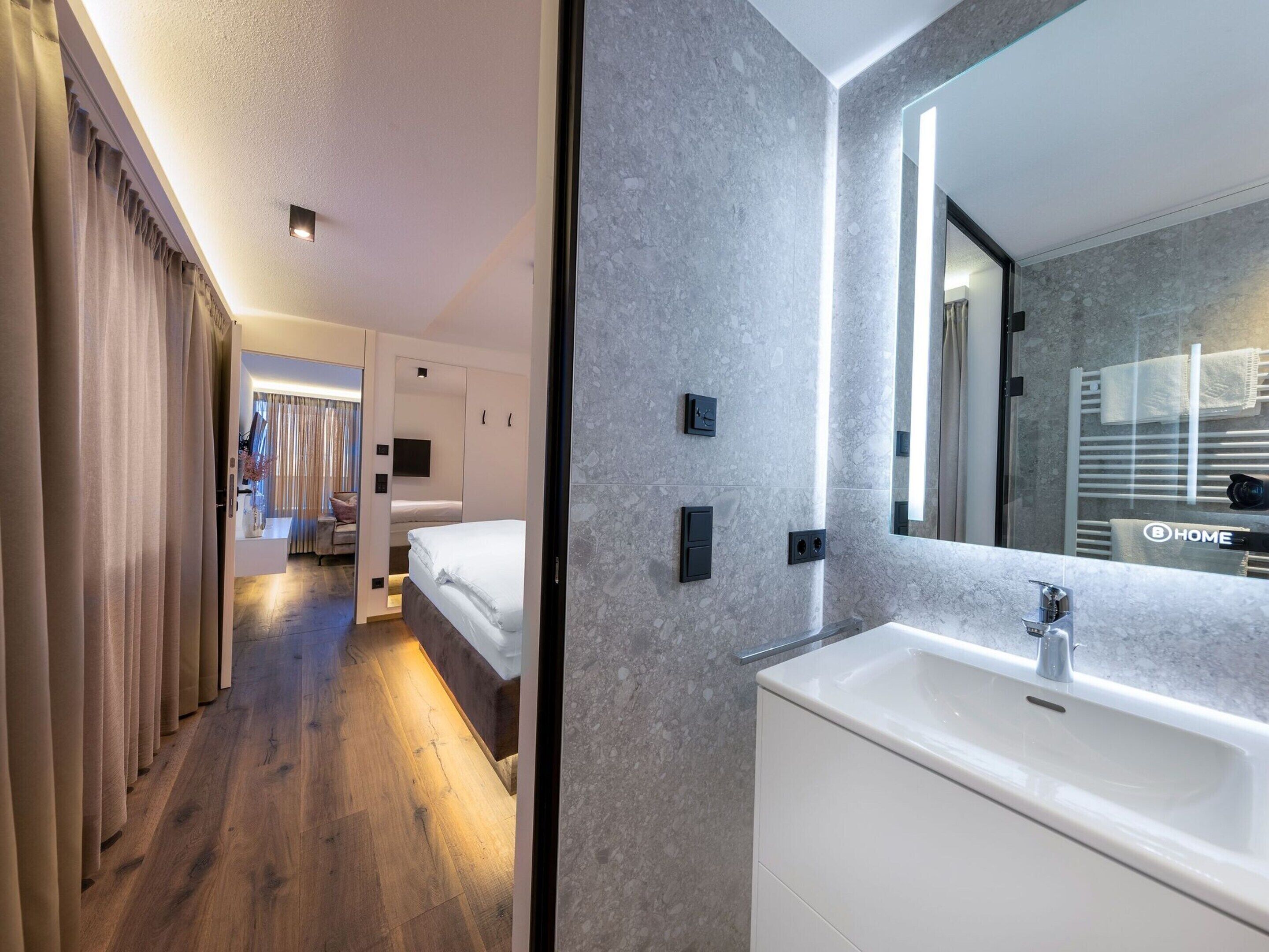 Ein modernes Hotelzimmer mit einem großen Spiegel, einem weißen Waschbecken und einem Holzboden.