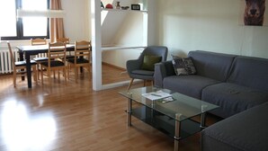 Una sala de estar moderna con una mesa de centro de vidrio, un sofá gris y un juego de comedor de madera.
