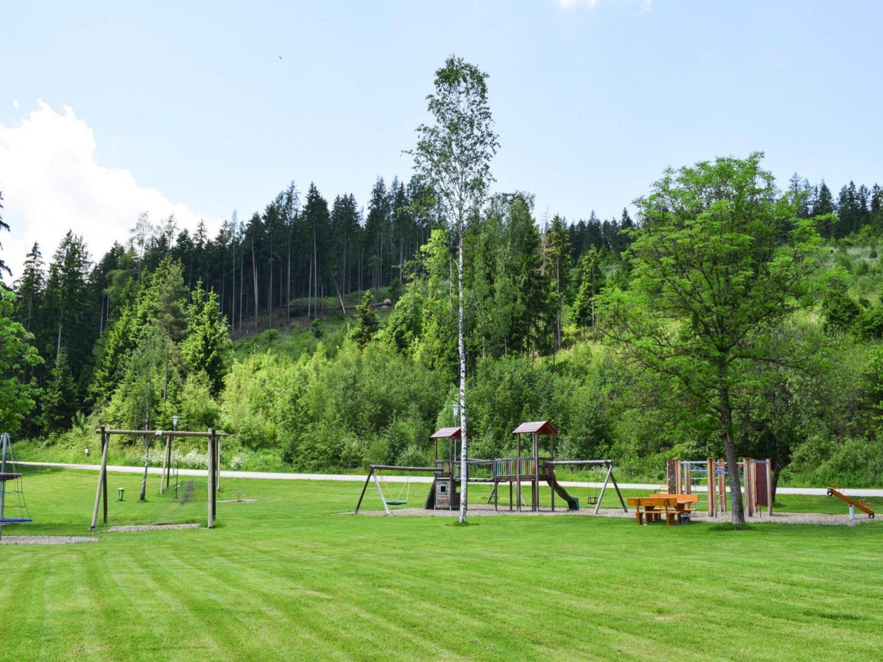 A playground with swings, slides, and a climbing structure surrounded by a grassy field and trees.