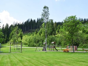 A playground with swings, slides, and a climbing structure surrounded by a grassy field and trees. - Hut Near Lake Traboch and Eisenerz Alps (Kammern im Liesingtal)