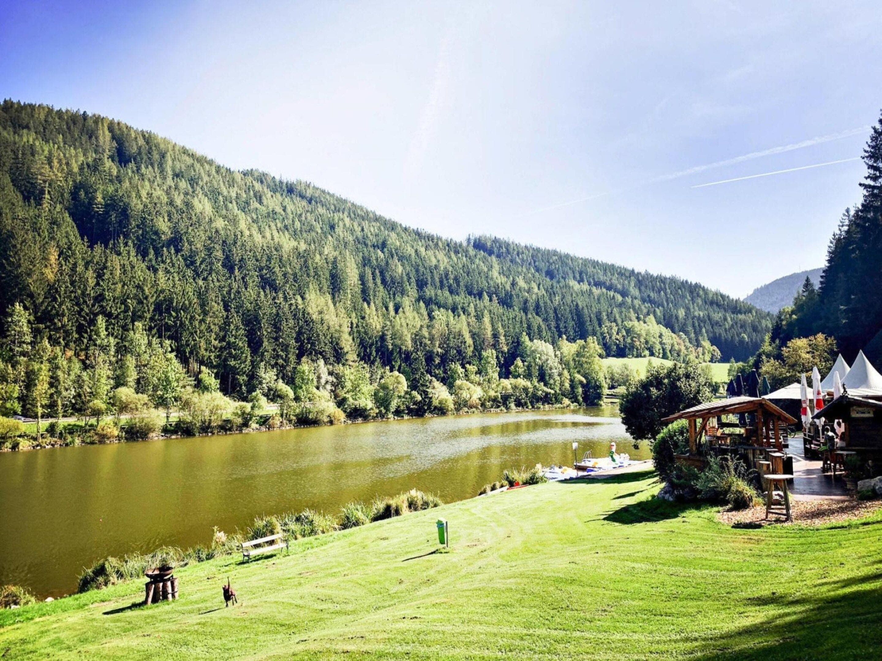 A lakeside view with a wooden cabin and a grassy area.
