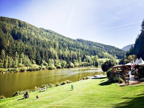 A lakeside view with a wooden cabin and a grassy area. - Hut Near Lake Traboch and Eisenerz Alps (Kammern im Liesingtal)