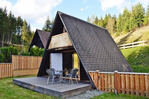 Eine Hütte mit geneigtem Dach, einer Terrasse mit Stühlen und einem Holzzaun.