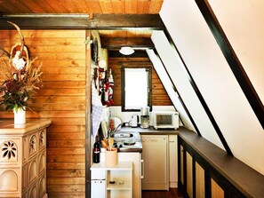 A compact kitchen with wooden walls, a white countertop, a microwave, a coffee maker, and a wine bottle. - Hut Near Lake Traboch and Eisenerz Alps (Kammern im Liesingtal)