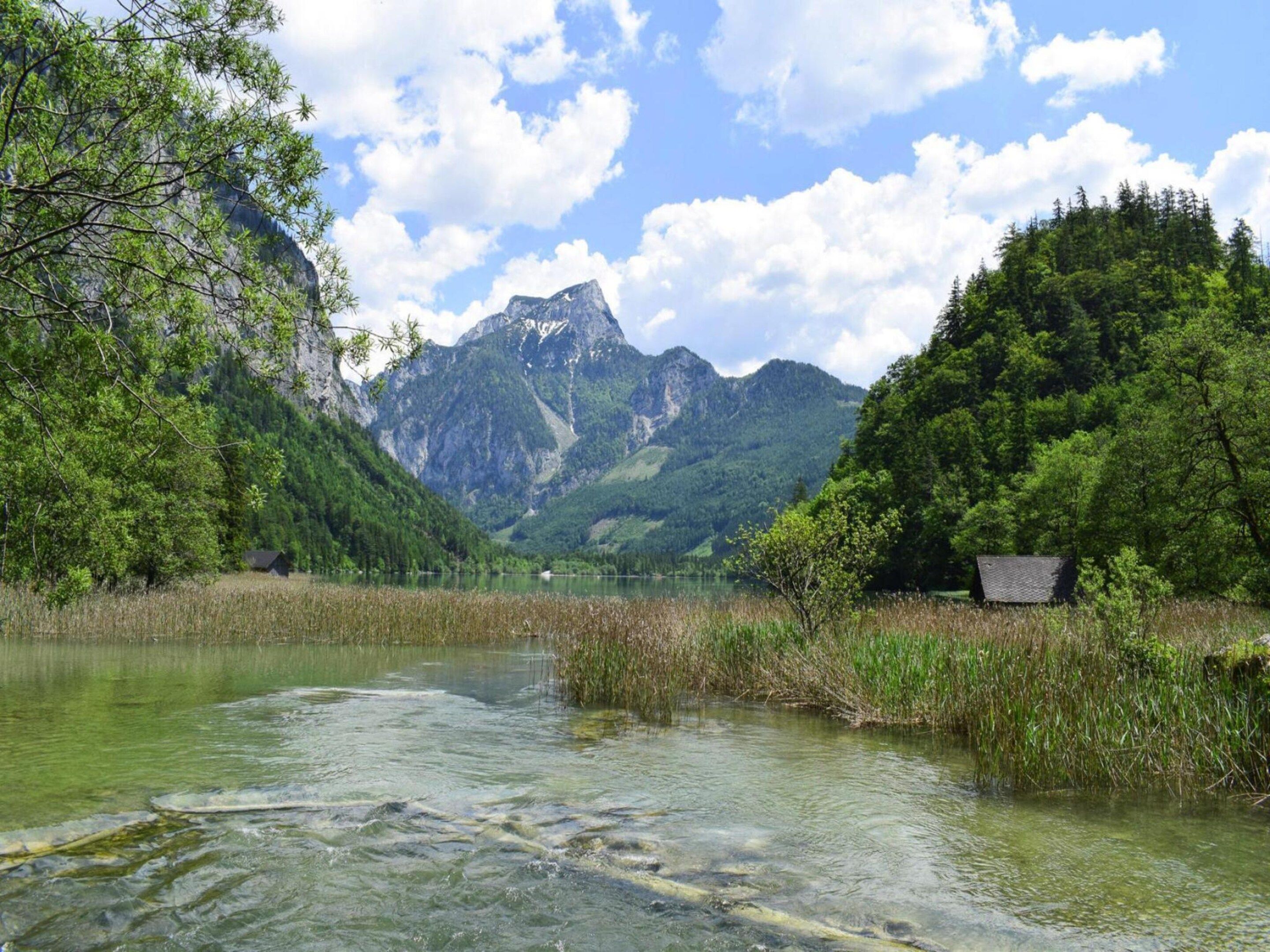 A clear mountain lake with a cabin on the right and a forested area on the left.