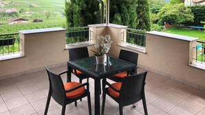 Un patio techado con una mesa y sillas, una orquídea en maceta y vistas a un paisaje verde.