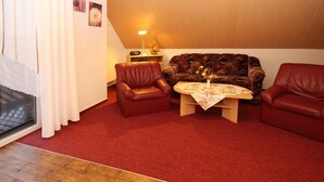 A cozy living room with a brown leather sofa, two red leather chairs, a wooden coffee table with a floral tablecloth, and a lamp on a side table. - Ferienwohnungen Spreewaldperle, Alt Zauche (Alt Zauche-Wußwerk)