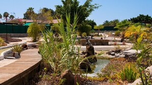 A landscaped garden with a wooden deck, a small pond, and various plants. - Central Bungalow With Communal Pool in Maspalomas (San Bartolomé de Tirajana)
