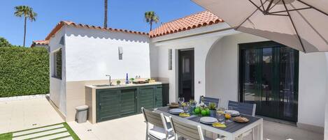 A patio with a dining table, chairs, and an umbrella. There is a small kitchen area with a sink and cabinets.