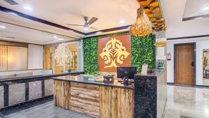 Un espace d’accueil doté d’un comptoir de réception en bois, d’un mur végétal orné d’un emblème décoratif, d’un ventilateur de plafond et d’un luminaire suspendu.