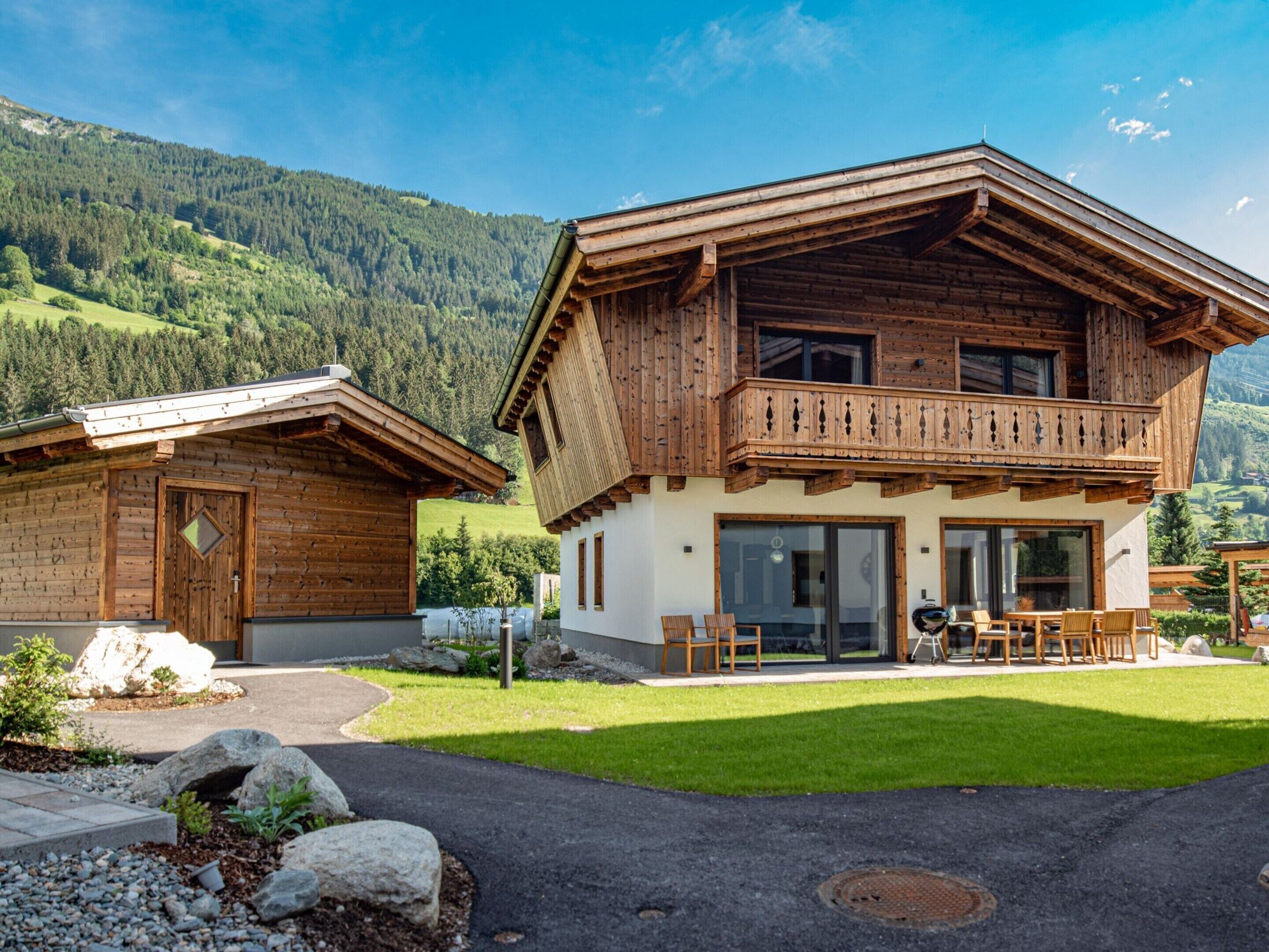Un chalet de madera de dos pisos con un balcón, entrada de piedra y vistas a un paisaje montañoso.
