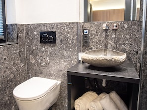 A modern bathroom with a marble backsplash, a stone basin sink, a toilet, and a towel rack.